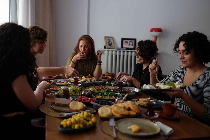 A group of people seated around a table with various dishes, including bread, salads, and drinks. 1