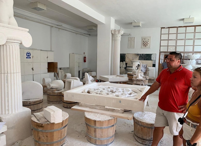 A workshop with marble sculptures, wooden barrels, and architectural columns. 4