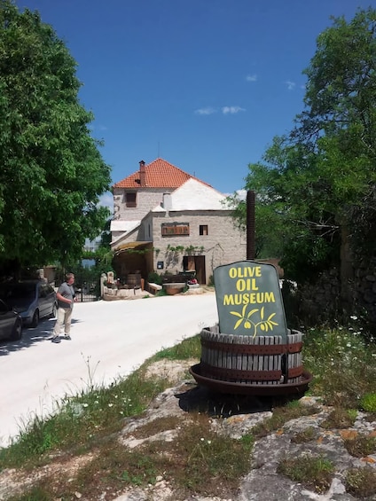 A stone building with a red roof, an olive oil museum sign, and a person standing in the foreground. 2