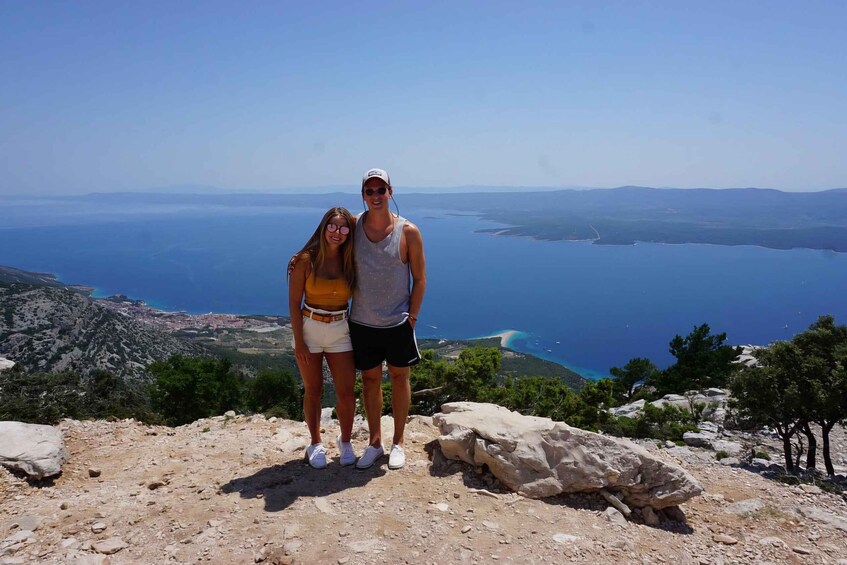Two people standing on a rocky outcrop with a view of a large body of water and distant land. 3