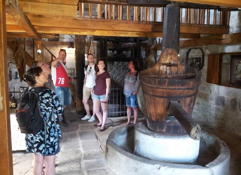 A group of people observing a large wooden mill with a water wheel. 5
