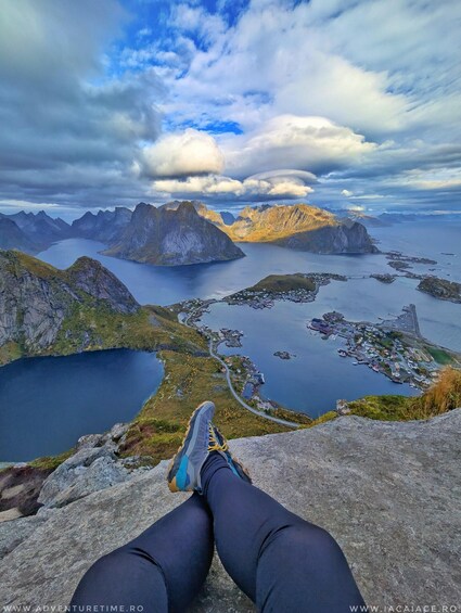 A person sitting on a cliff overlooking a fjord with mountains and a small town. 3
