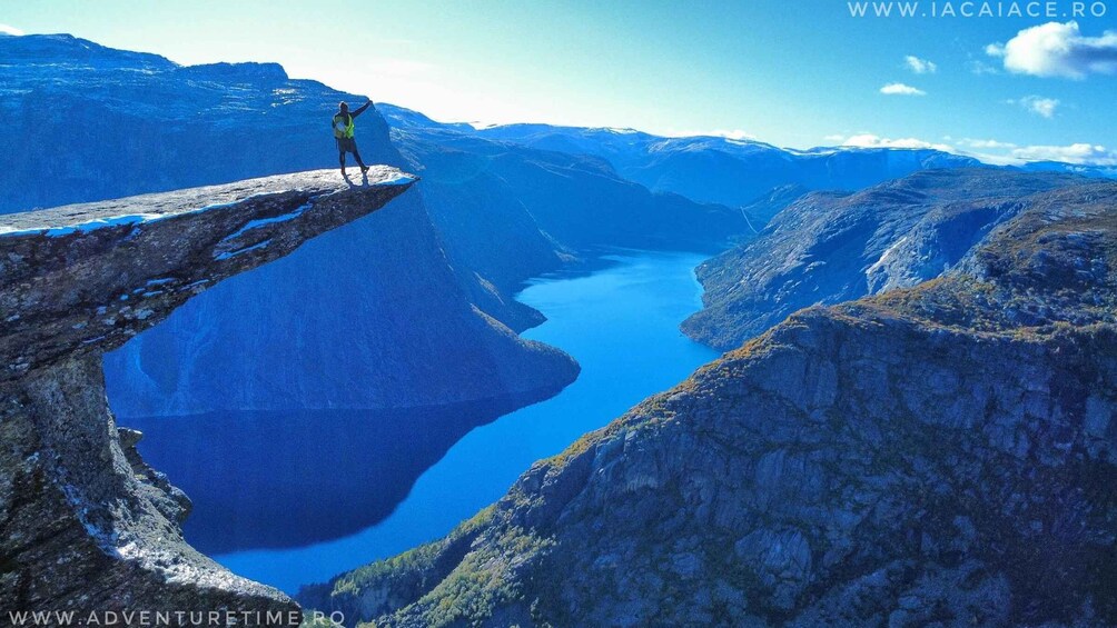 A person standing on a cliff edge overlooking a deep blue lake surrounded by rugged terrain. 2