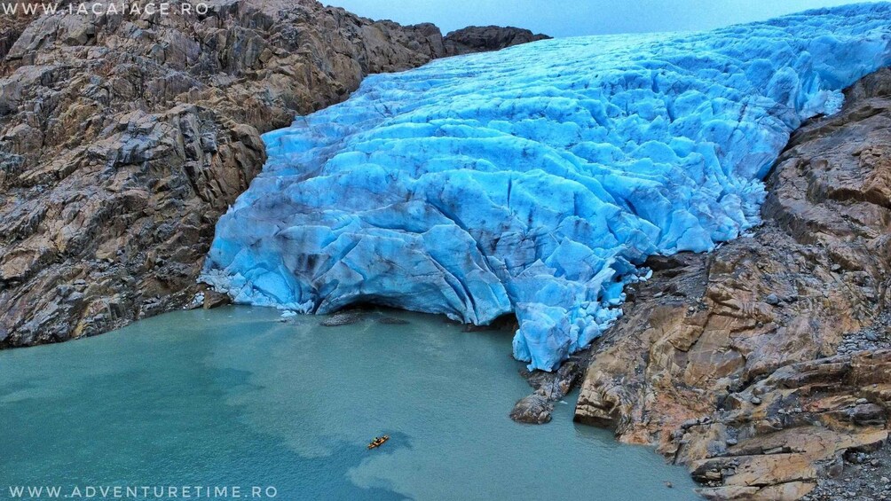 A glacier with blue ice, rocky terrain, and a body of water. 1