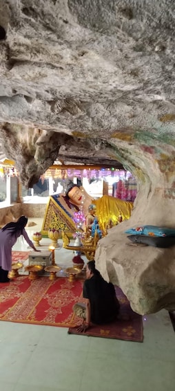 A cave interior with a statue of a deity, a seated figure, and a person performing a ritual. 5