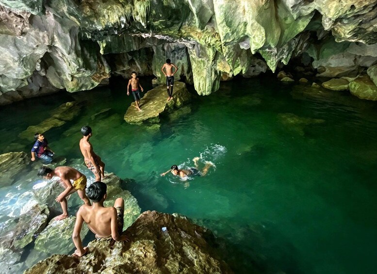Un grupo de personas nadando y paradas sobre rocas en una cueva con agua cristalina. 1
