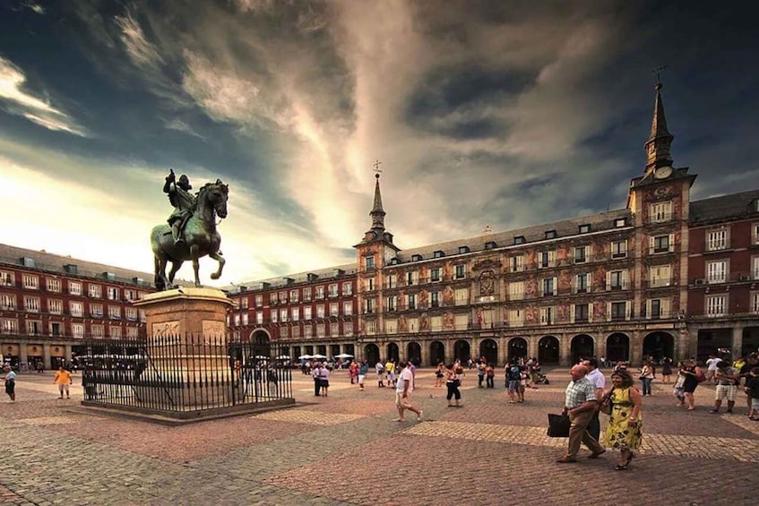 A historic plaza with a statue, buildings, and a cloudy sky. 2