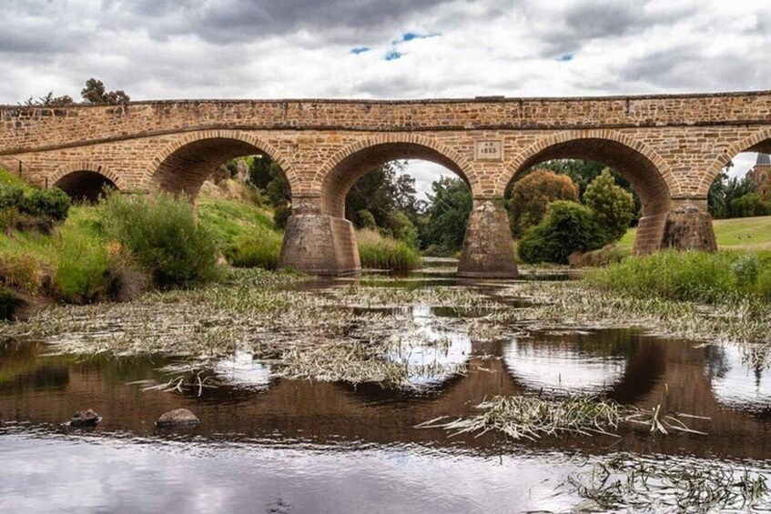 A stone bridge with multiple arches over a calm river, surrounded by greenery. 4