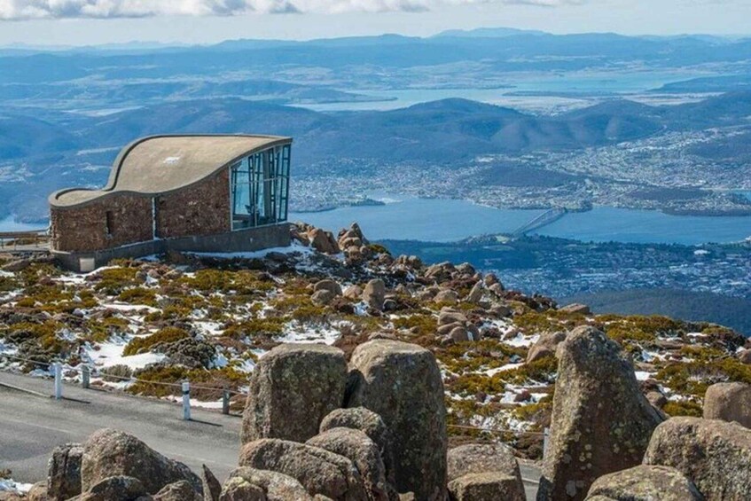 A modern building with a curved roof overlooking a mountainous landscape with a lake and a bridge. 1