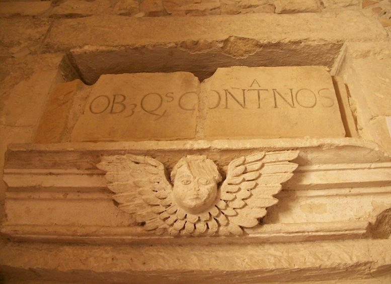 A stone carving with the inscription 'A OBQOS CONTNOS' and an angelic figure with wings. 5