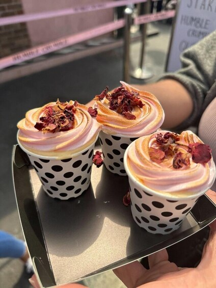 Three polka-dotted cups with whipped cream and dried rose petals on a tray. 4