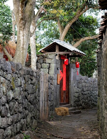 A traditional stone-walled structure with a wooden door, a thatched roof, and red decorations. 4