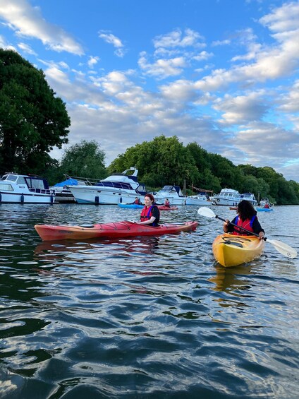 Kayakers on a calm river with boats docked on the shore and trees lining the banks. 2