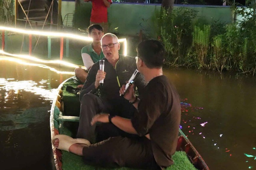 A boat with people sitting on it, a water body, and some greenery in the background. 5
