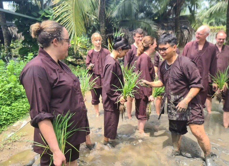 A group of people in a muddy outdoor setting, some holding plants. 1