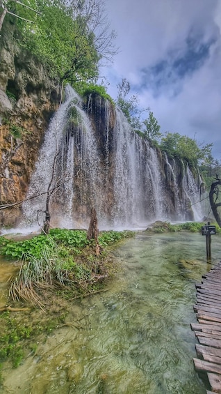 A waterfall cascading over a rocky cliff into a clear pool, surrounded by greenery. 2