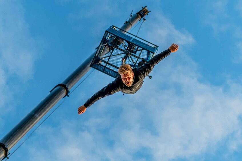 A person skydiving with outstretched arms, a clear blue sky, and a tall metal structure in the background. 5