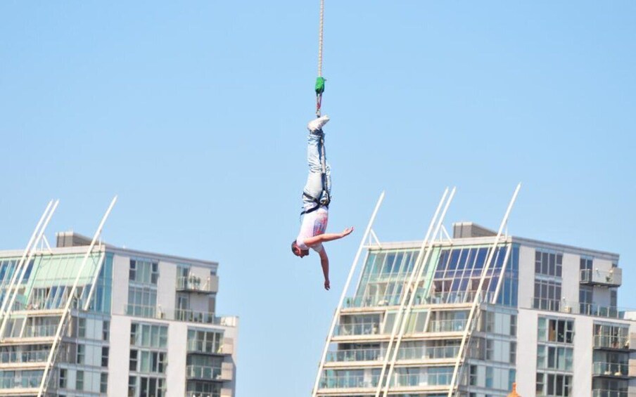 A person performing an aerial stunt, suspended by a rope, with modern buildings in the background. 4