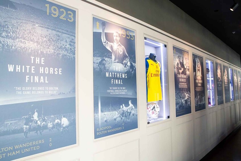 A wall with framed historical football match posters and a yellow jersey. 2