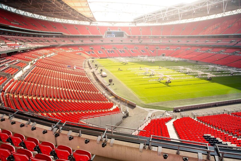 A large stadium with red seats and a green field, including a large screen displaying 'ICONS.' 5