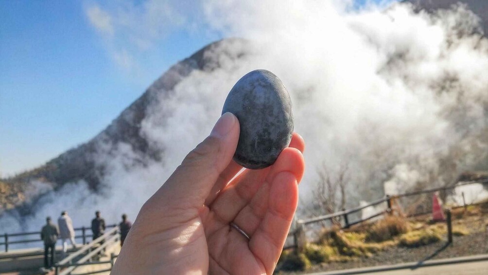 A hand holding a smooth, rounded stone with a mountainous background and steam rising from the ground. 5