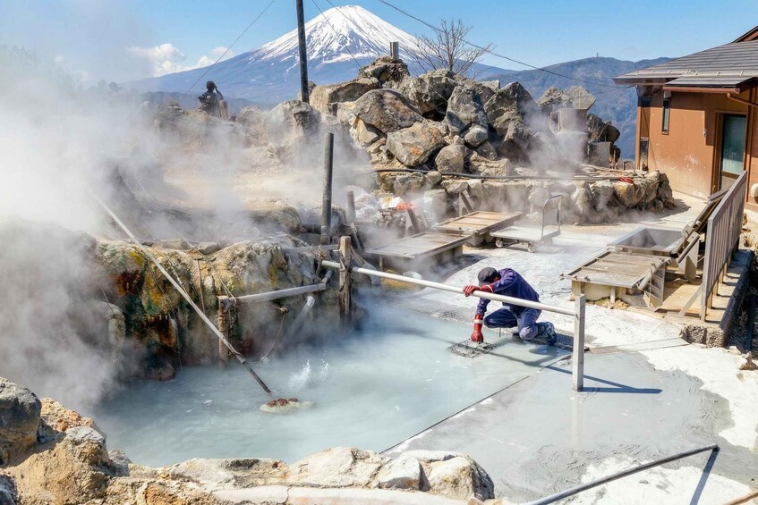 A hot spring area with steam rising, a wooden walkway, and a mountain in the background. 2