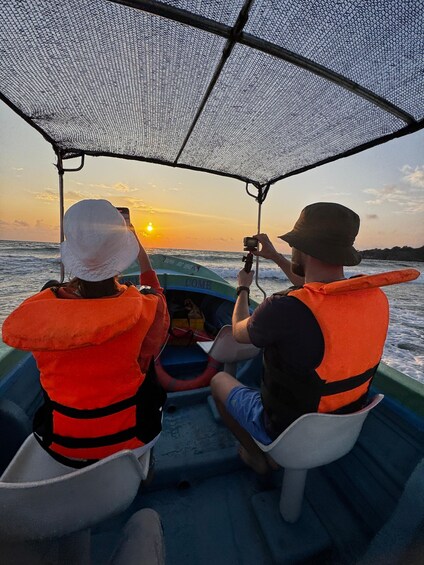 Twee mensen in een boot, met reddingsvesten, met een zonsondergang op de achtergrond. 3
