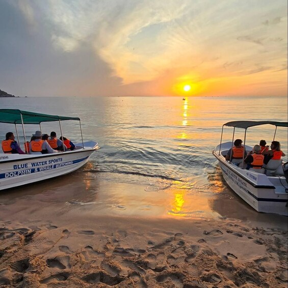 Twee boten met mensen in reddingsvesten op een strand bij zonsondergang. 1