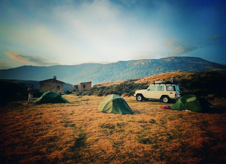 En campingplats med tält, ett fordon och en bergig bakgrund. 2