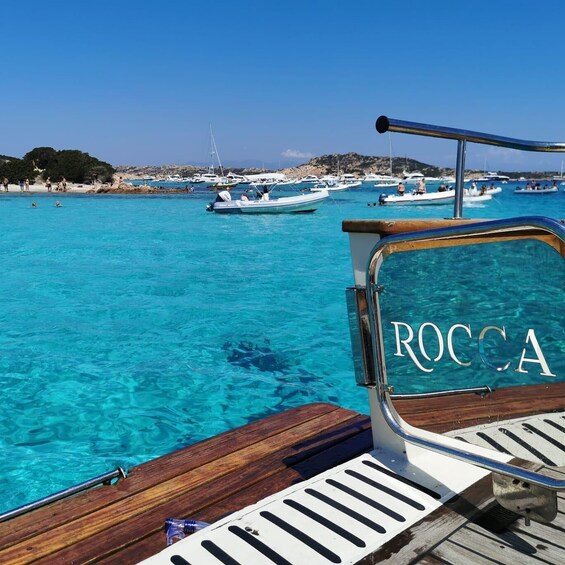 A boat deck with the name 'ROCCA' and clear turquoise water with boats in the background. 5