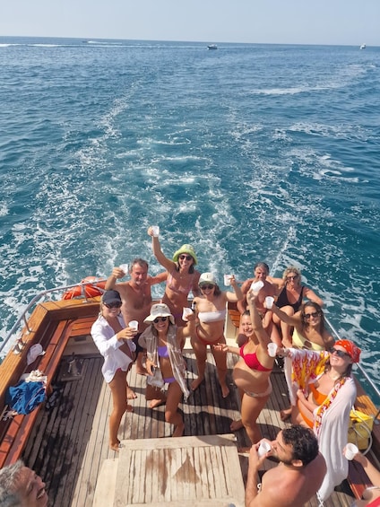 A group of people on a wooden boat in the ocean, holding cups and smiling. 2