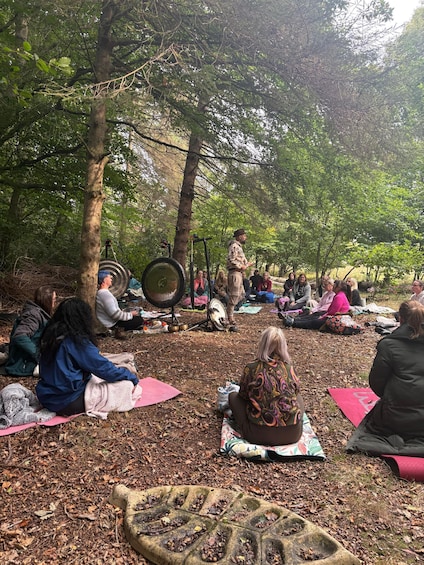 People sitting on mats in a forested area, some with musical instruments. 5