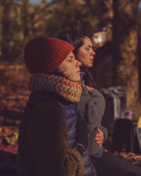 Two people sitting outdoors, one wearing a red beanie and a multicolored scarf, the other in a grey sweater. 4