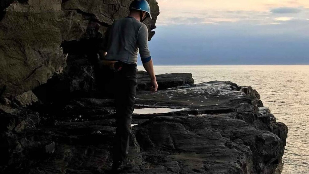A person climbing a rocky cliff by the sea. 4