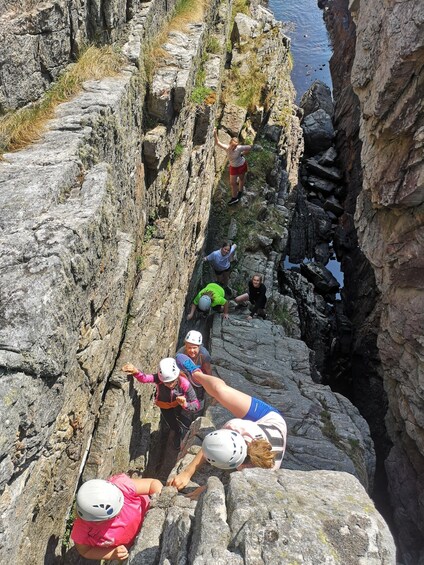 A group of people rock climbing on a rocky cliff by the sea. 2