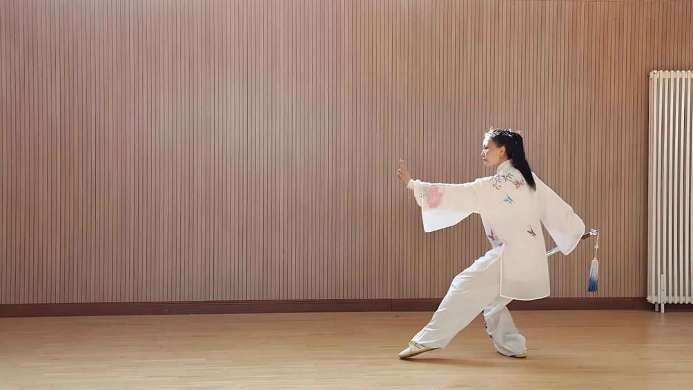 A person performing Tai Chi in a room with wooden paneling and a radiator. 2
