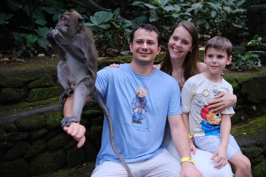 A family with a monkey, sitting on a moss-covered stone wall in a natural setting. 2