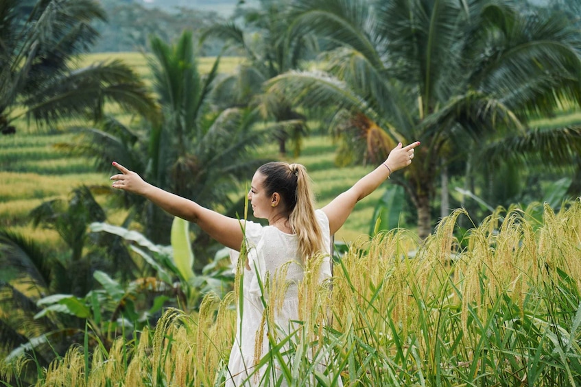 A person standing in a field with arms raised, surrounded by tall grass and palm trees. 3