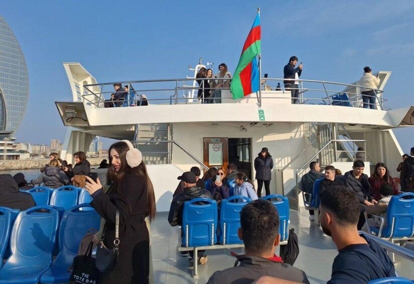 A ferry with passengers seated and standing, a flag, and a modern building in the background. 3