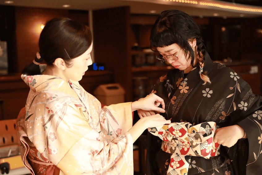 Due persone vestite con abiti tradizionali giapponesi, una con un kimono chiaro a motivi floreali e l'altra con un kimono scuro a motivi floreali e geometrici. 1