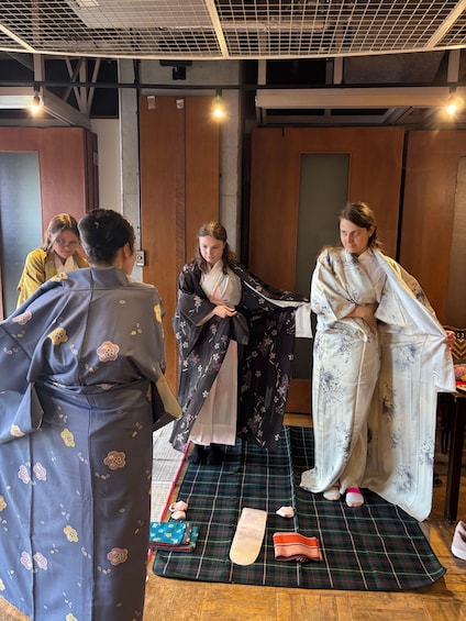 Un gruppo di persone in abiti tradizionali, probabilmente in preparazione a un evento culturale o a una cerimonia, con tappeti e accessori sul pavimento. 5