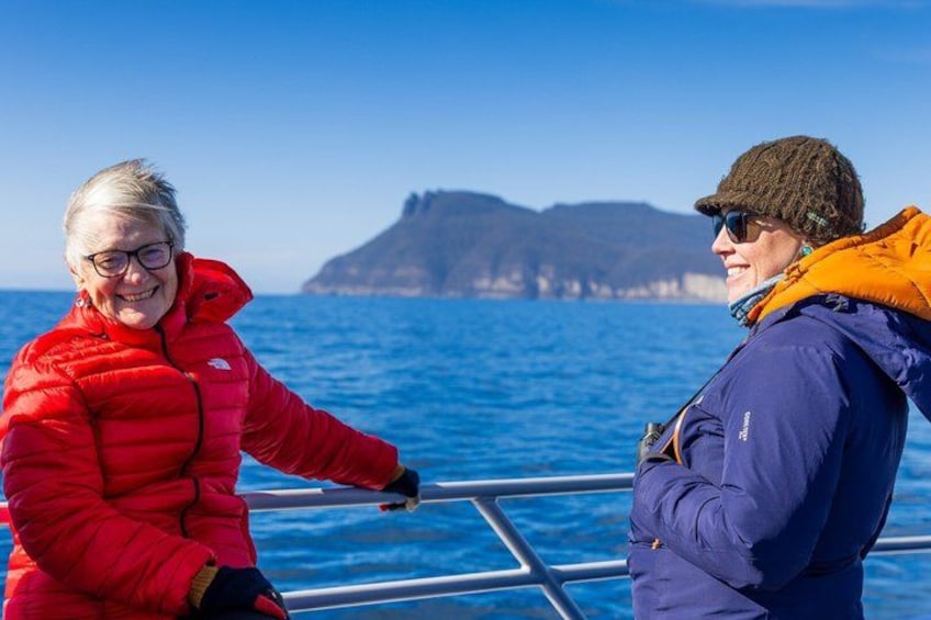 Two people on a boat with a mountainous coastline in the background. 2