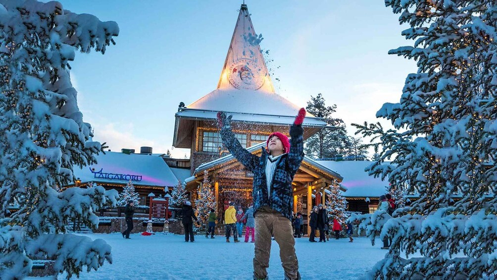 A person in a snowy outdoor setting with a building featuring a pointed roof and illuminated windows. 4