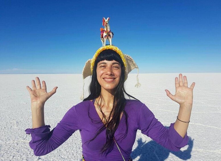 Una persona con remera morada, con los brazos levantados, parada en un extenso paisaje blanco bajo un cielo azul despejado. 4