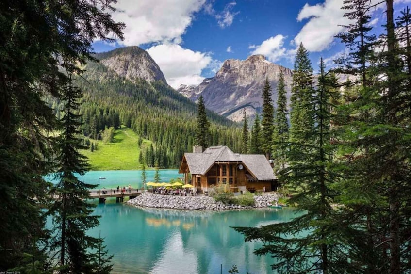 A lodge by a turquoise lake surrounded by forest and mountains. 1
