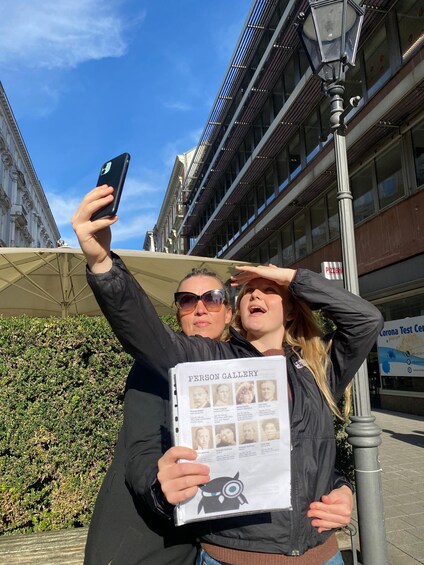 Two people taking a selfie with a person gallery book. 2