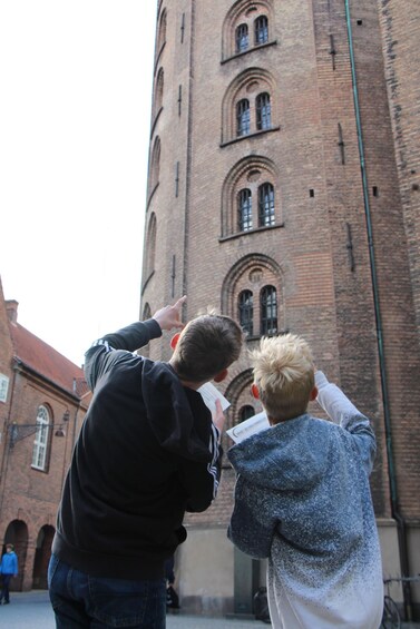 Three people looking at a tall brick building with arched windows. 1