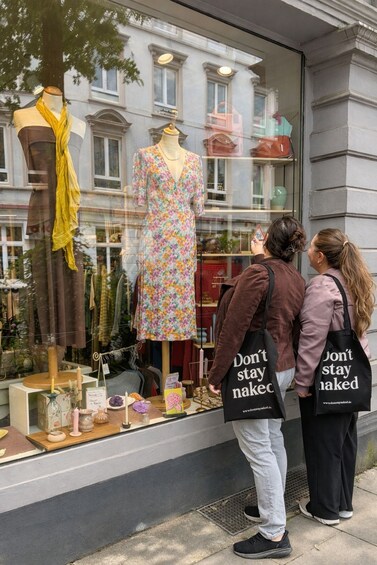 Two people looking at a store window with a mannequin in a floral dress and a yellow scarf. 2