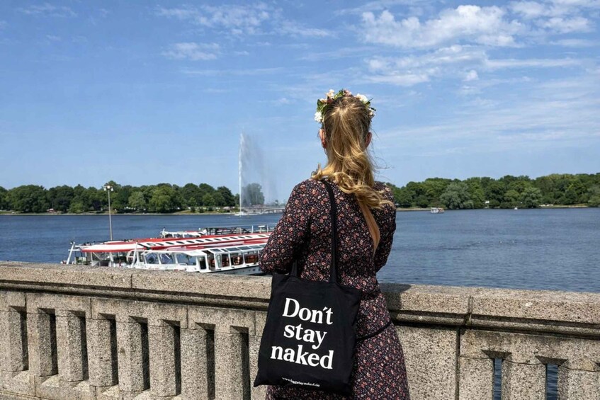 A woman with a floral headpiece standing by a river with a boat and a fountain in the background. 1