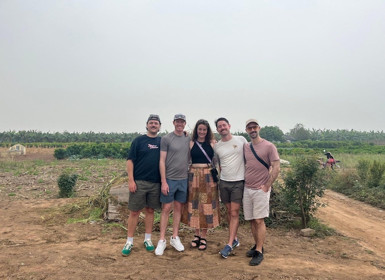 A group of five people standing on a dirt path with a rural landscape in the background. 3